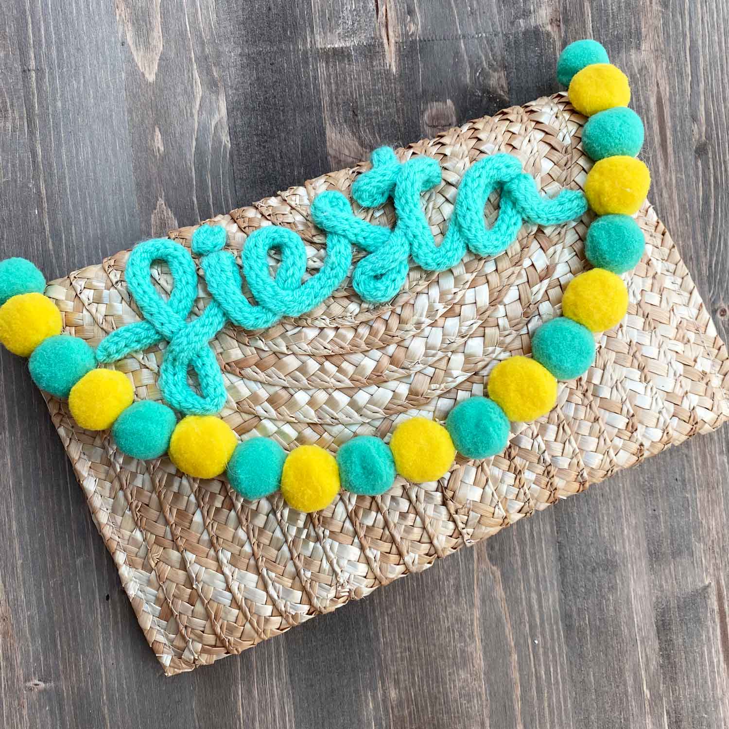 Pochette in paglia Ibiza con scritta personalizzata e pon pom gialli/azzurri